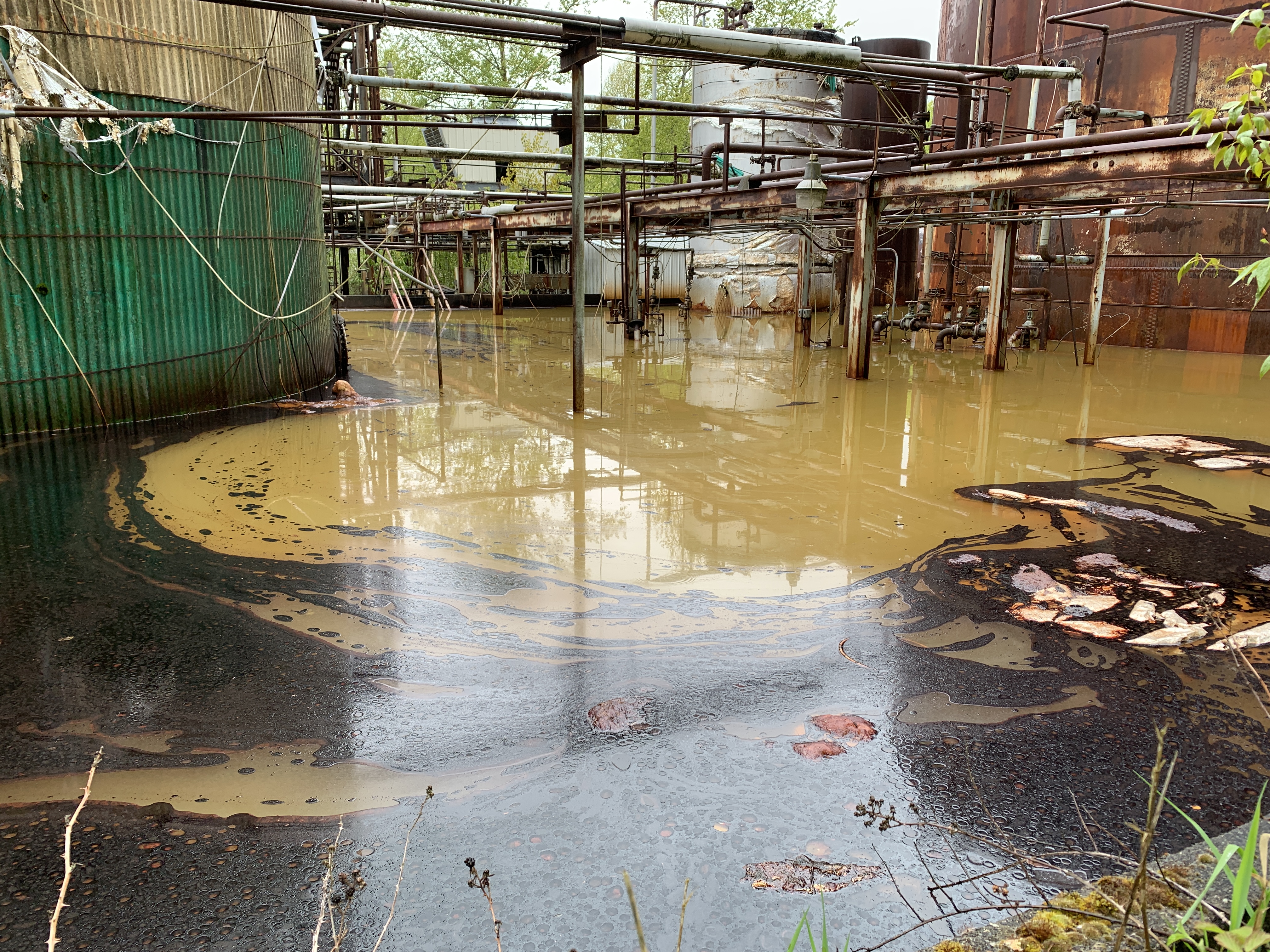 Large tanks stand in a pool of oily liquid.