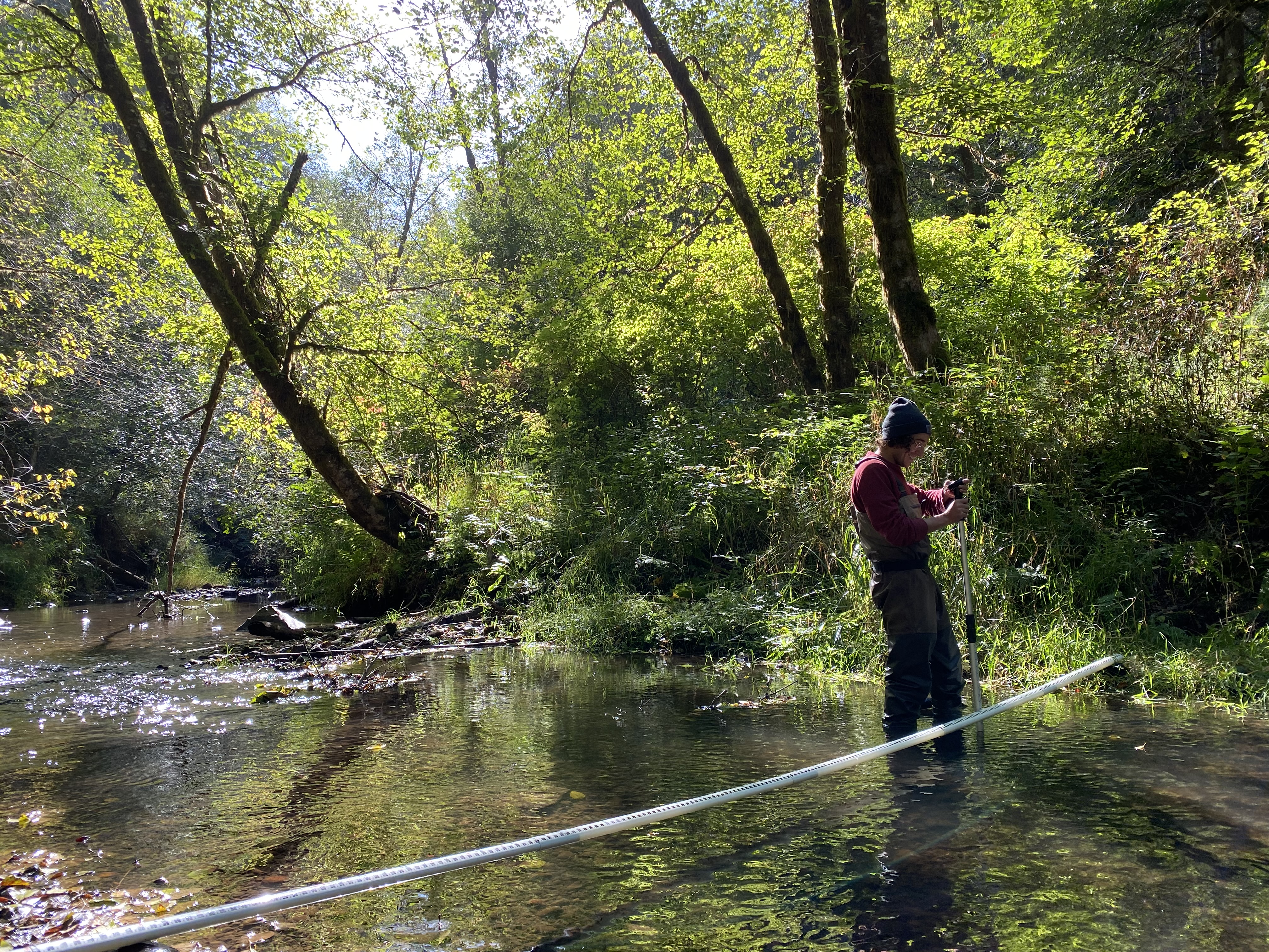 Person standing in a stream uses a long rod to record measure channels in a stream