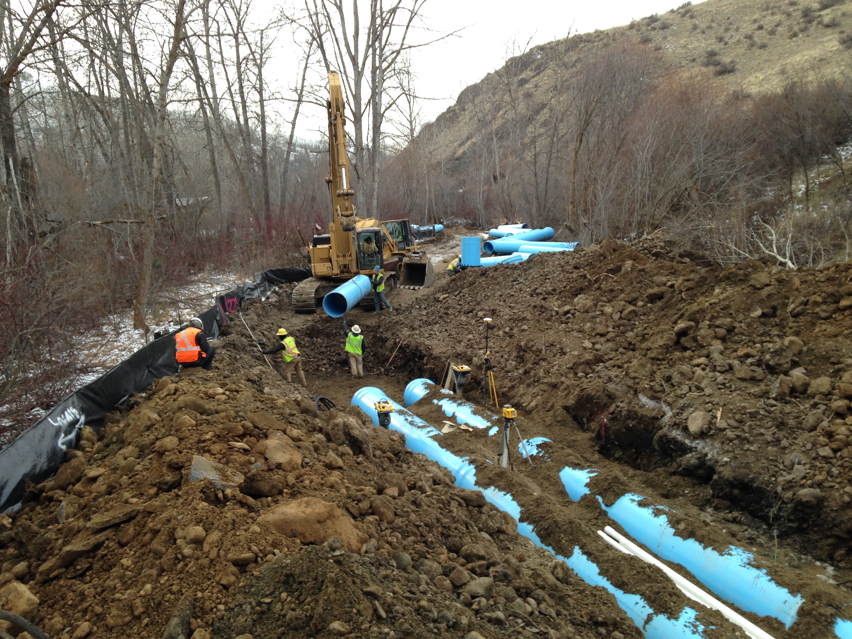 Large blue irrigation pipe is entrenched in the ground next to flowing creek