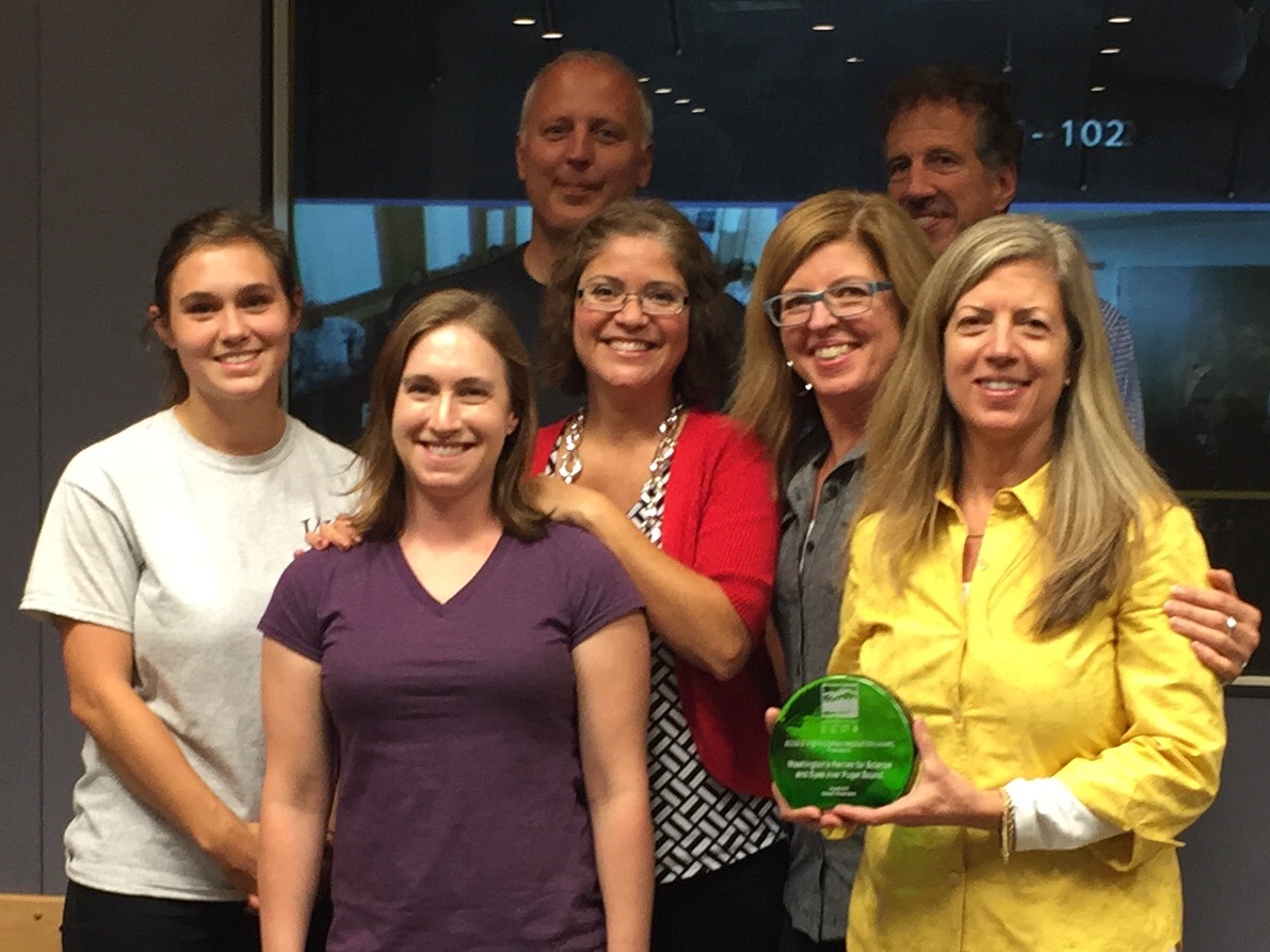 Six scientists stand with Maia Bellon. One scientist holds a green glass award. 