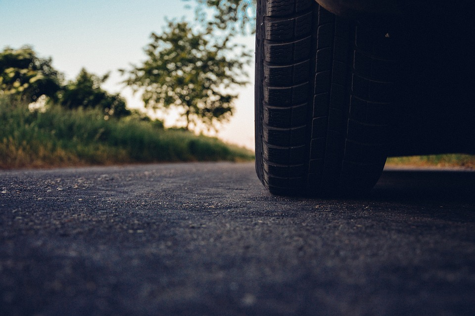 A zoomed-in photo of a vehicle tire on a road surrounded by tall grass.