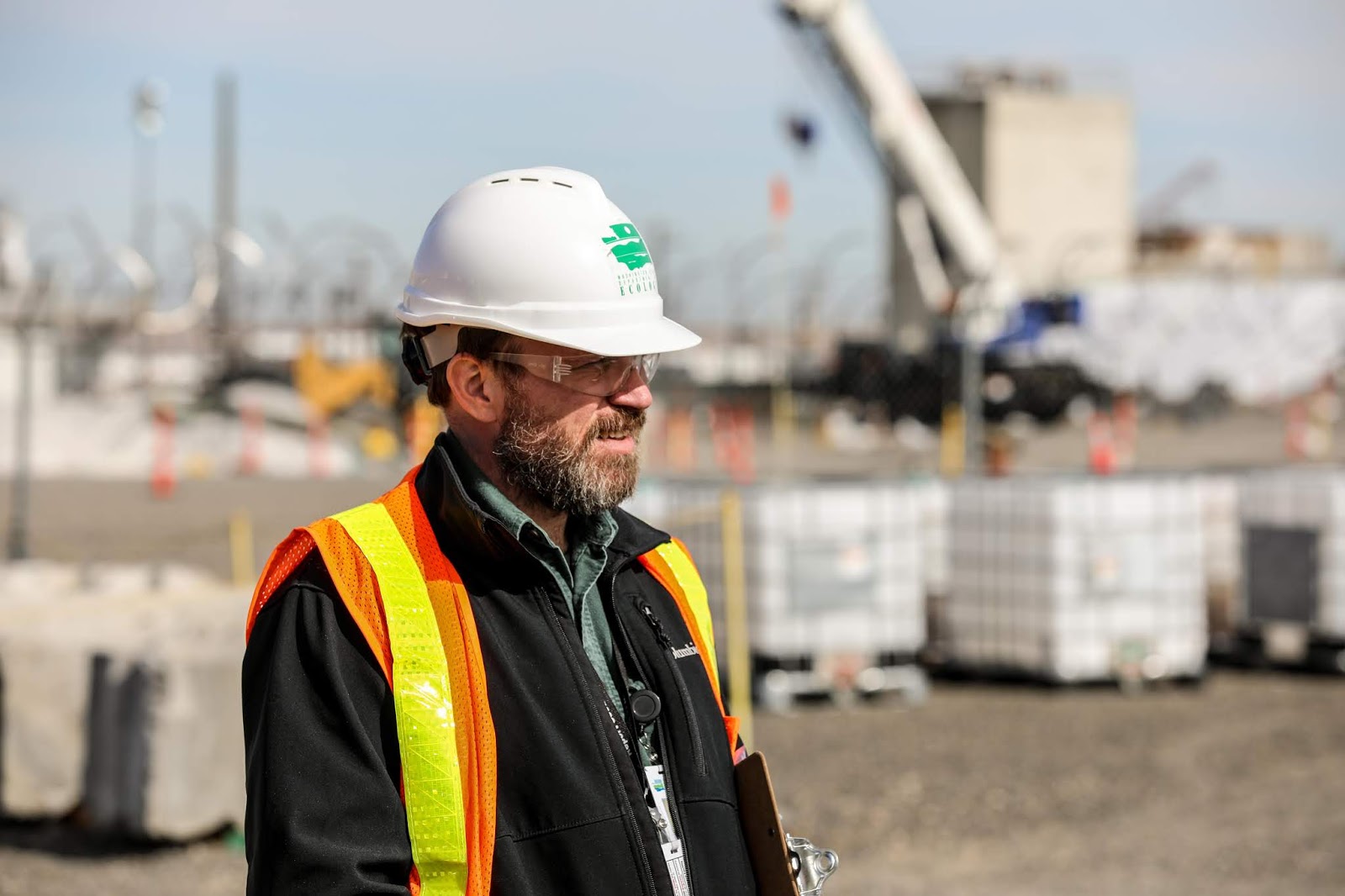 A man stands near one of Hanford's PUREX tunnels. He wears a construction helmet, safety glasses and a vest.
