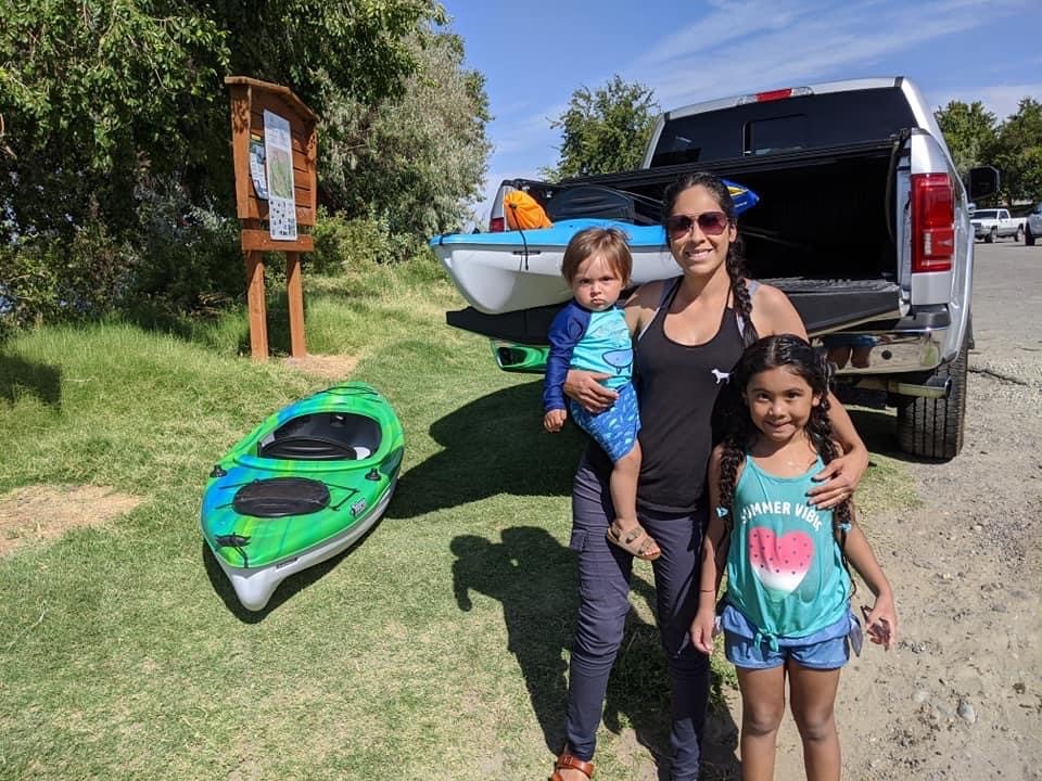 Woman with two children standing in front of a truck with kayaks.