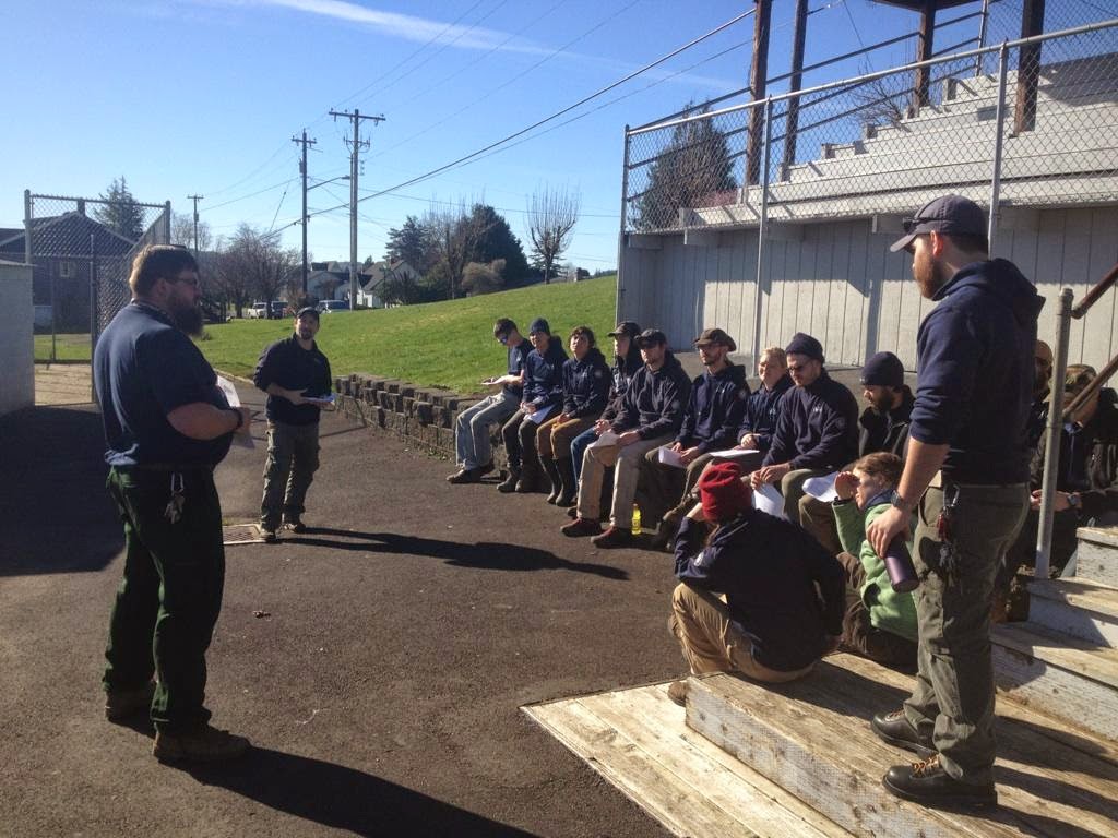 A crew supervisor addresses a group of AmeriCorps members sitting on some bleachers.