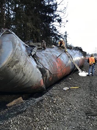 Responders standing next to a derailed tank car.