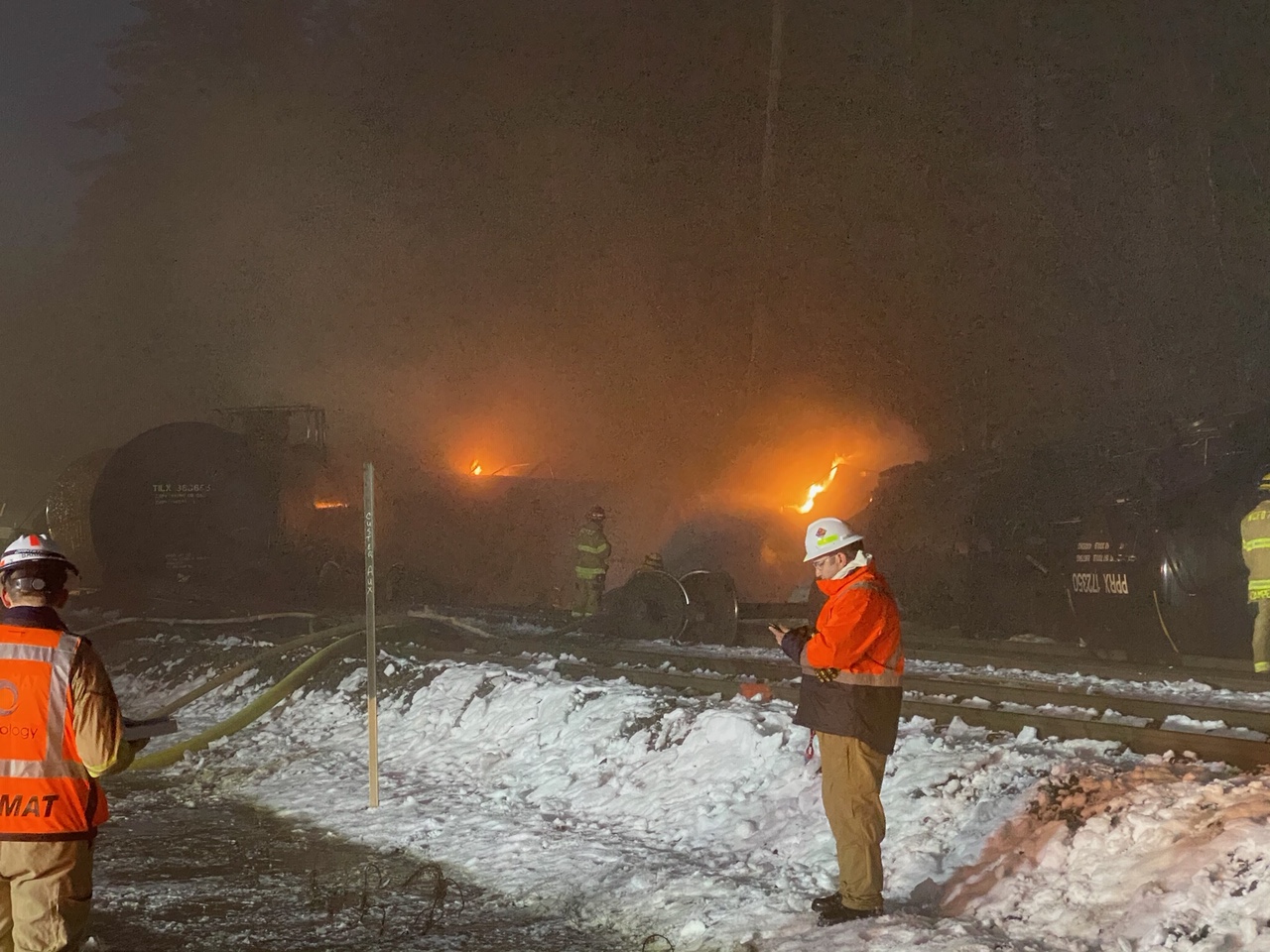 Firefighters in front of a derailed train on fire at night