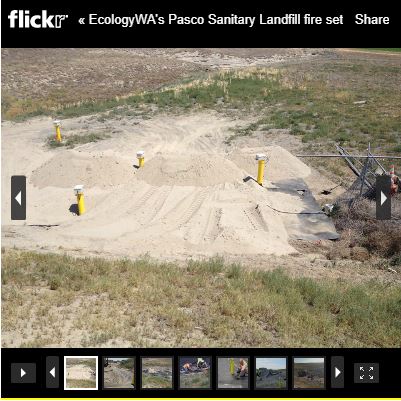 Part of Pasco Landfill, showing a large dirt pile with broken fence on side, four yellow pilings in dirt.