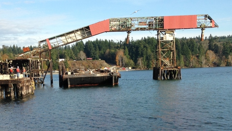 Port Gamble cleanup, equipment in water and workers standing on a dock.