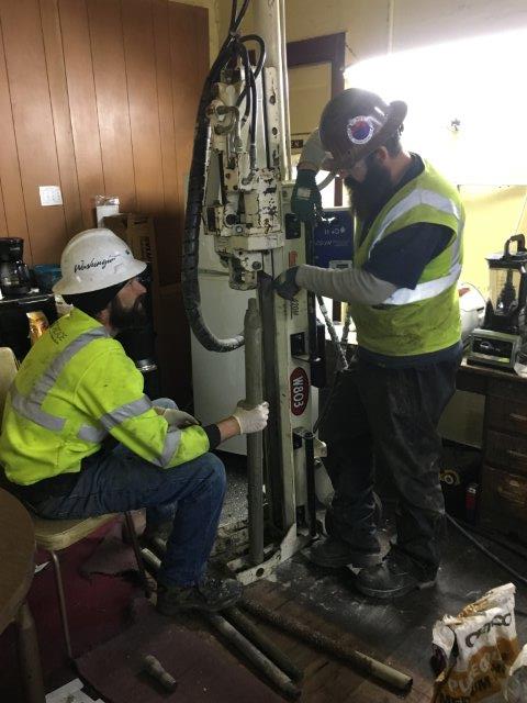 Two men operating a drilling rig inside the former dry cleaner building