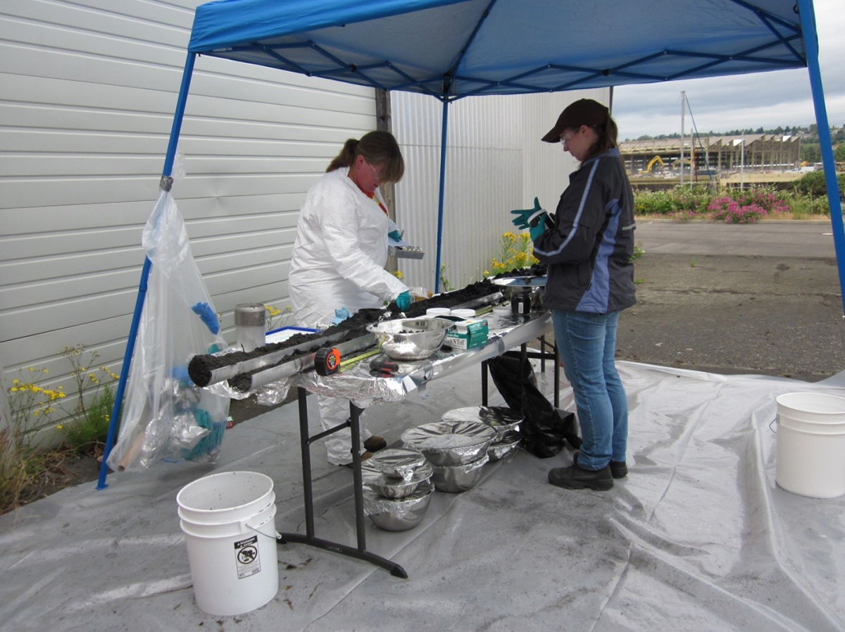Women in gloves measuring long narrow cylinders of sediment. 