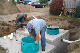 two men working to installing two septic tanks into the ground.