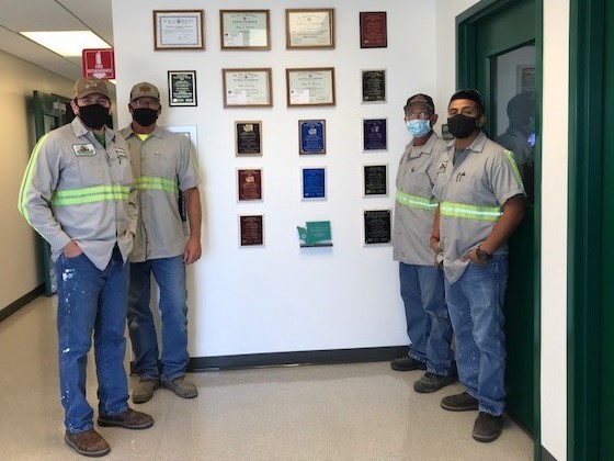 4 wastewater operators stand next to a wall filled with awards