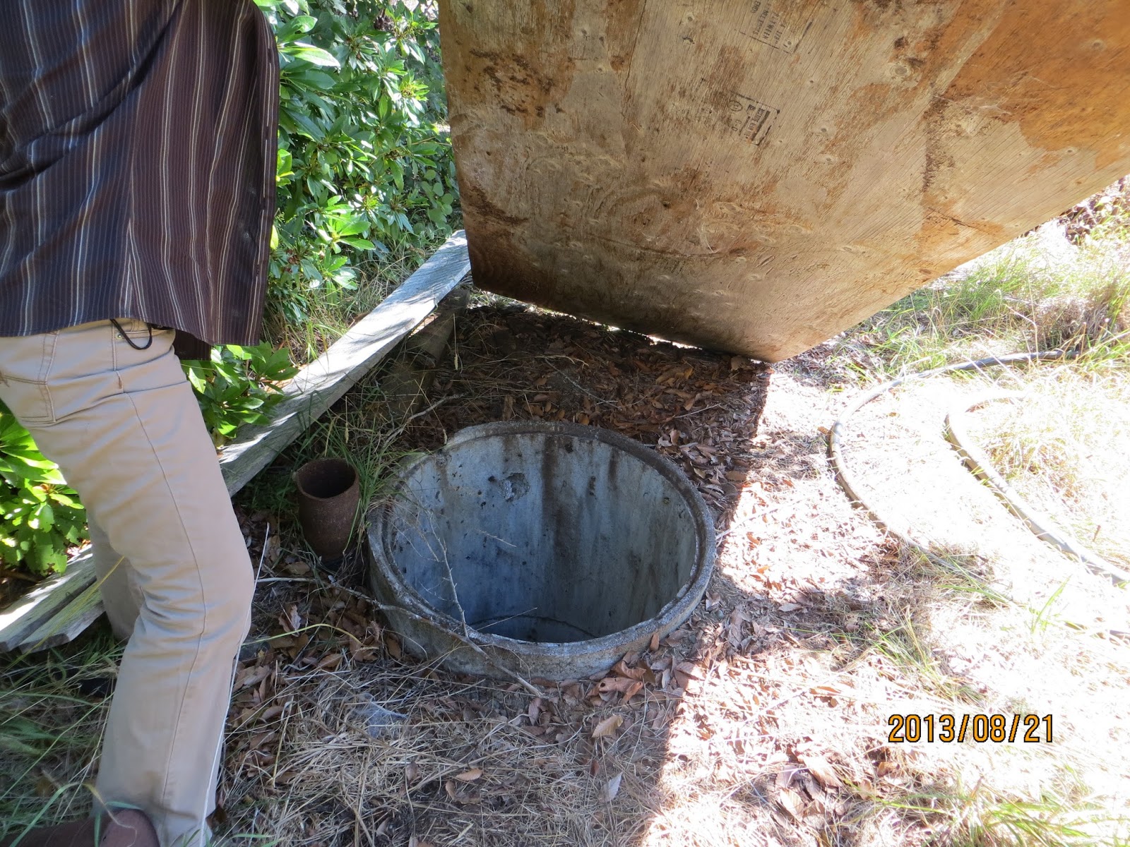 Man lifts a board of wood above an exposed well