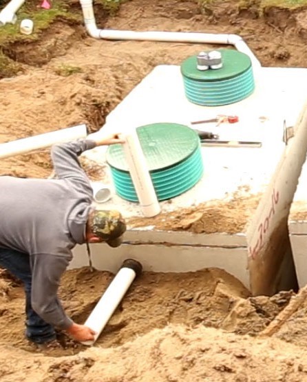 A hole is dug around a septic tank as a man inspects it