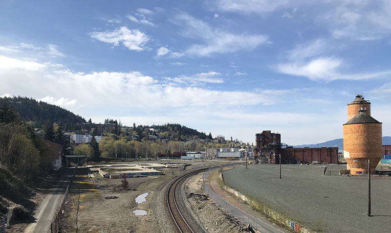 Railroad tracks run in a near-vertical line along the center of the photo. A building foundation is on the left of the tracks.