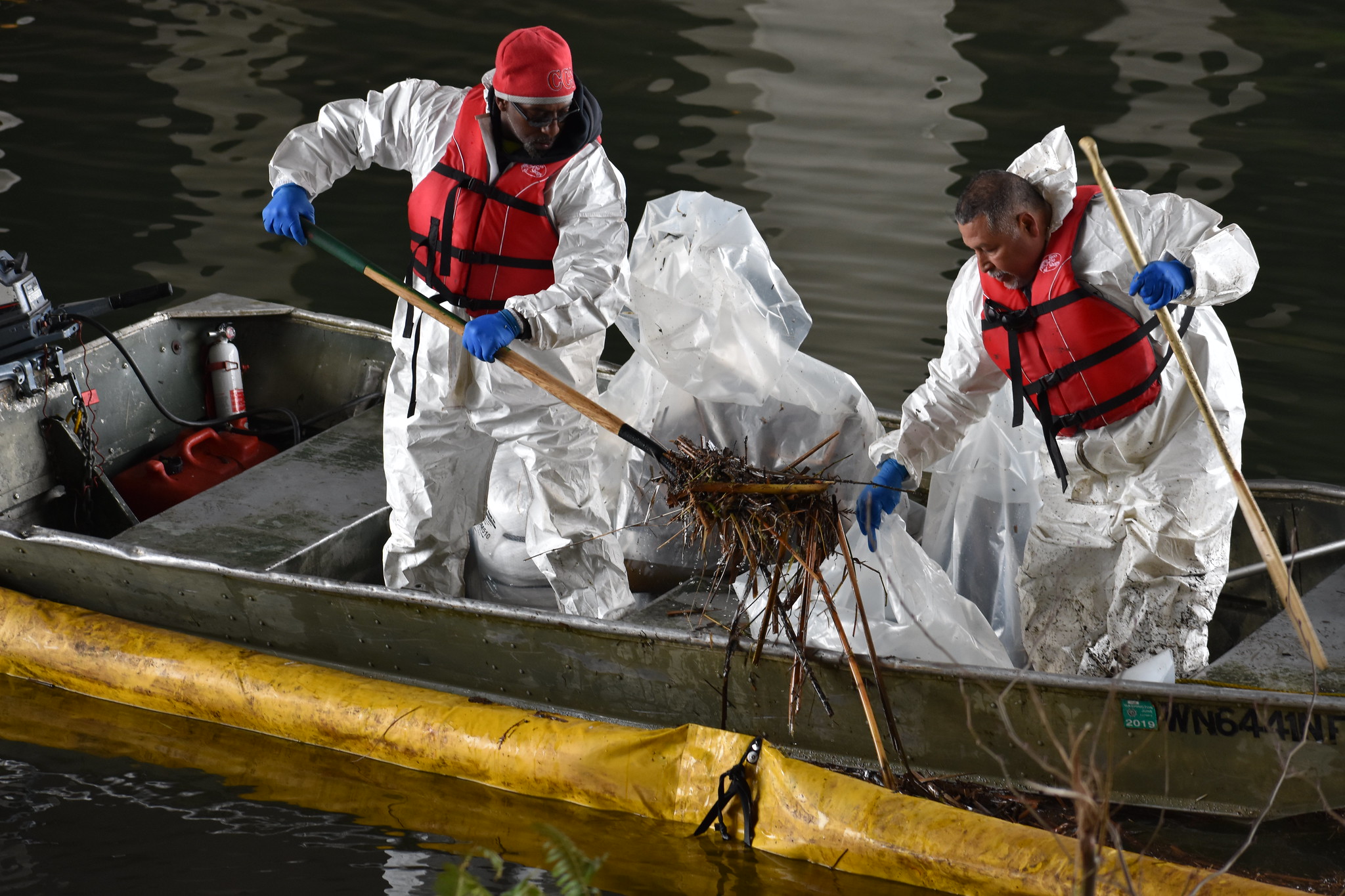 Two spill responders in a boat collecting oiled debris.