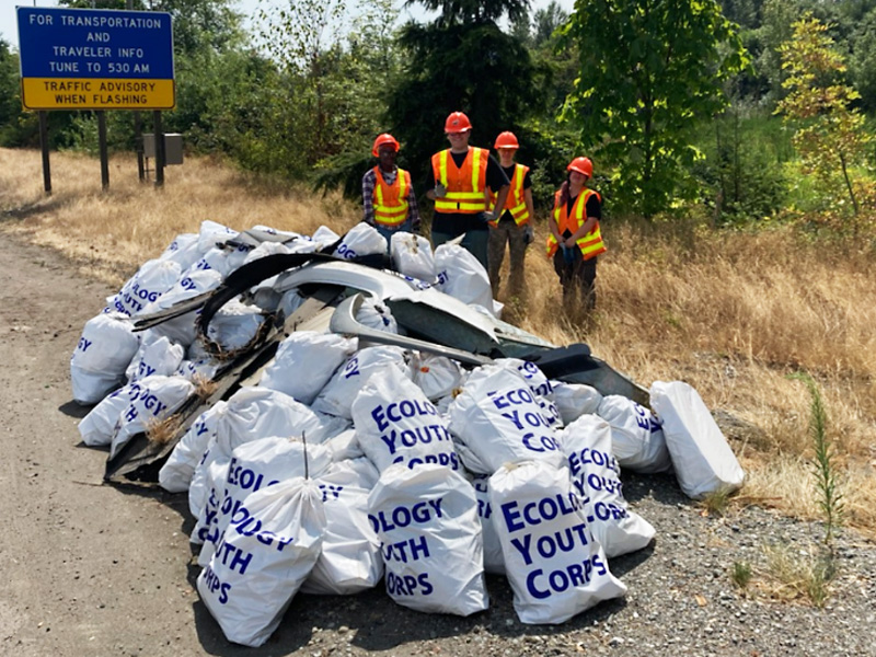An Ecology Youth Corps crew poses next to a pile of white and blue litter bags.