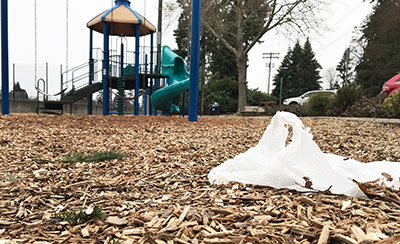A littered plastic bag lies partially buried beneath woodchips of an empty playground.