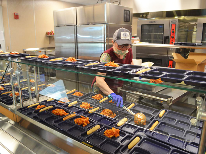 A school cafeteria worker places lunch items on durable, reusable trays.