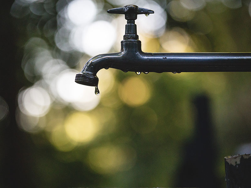 An outdoor water faucet with drip of water and blurry background.