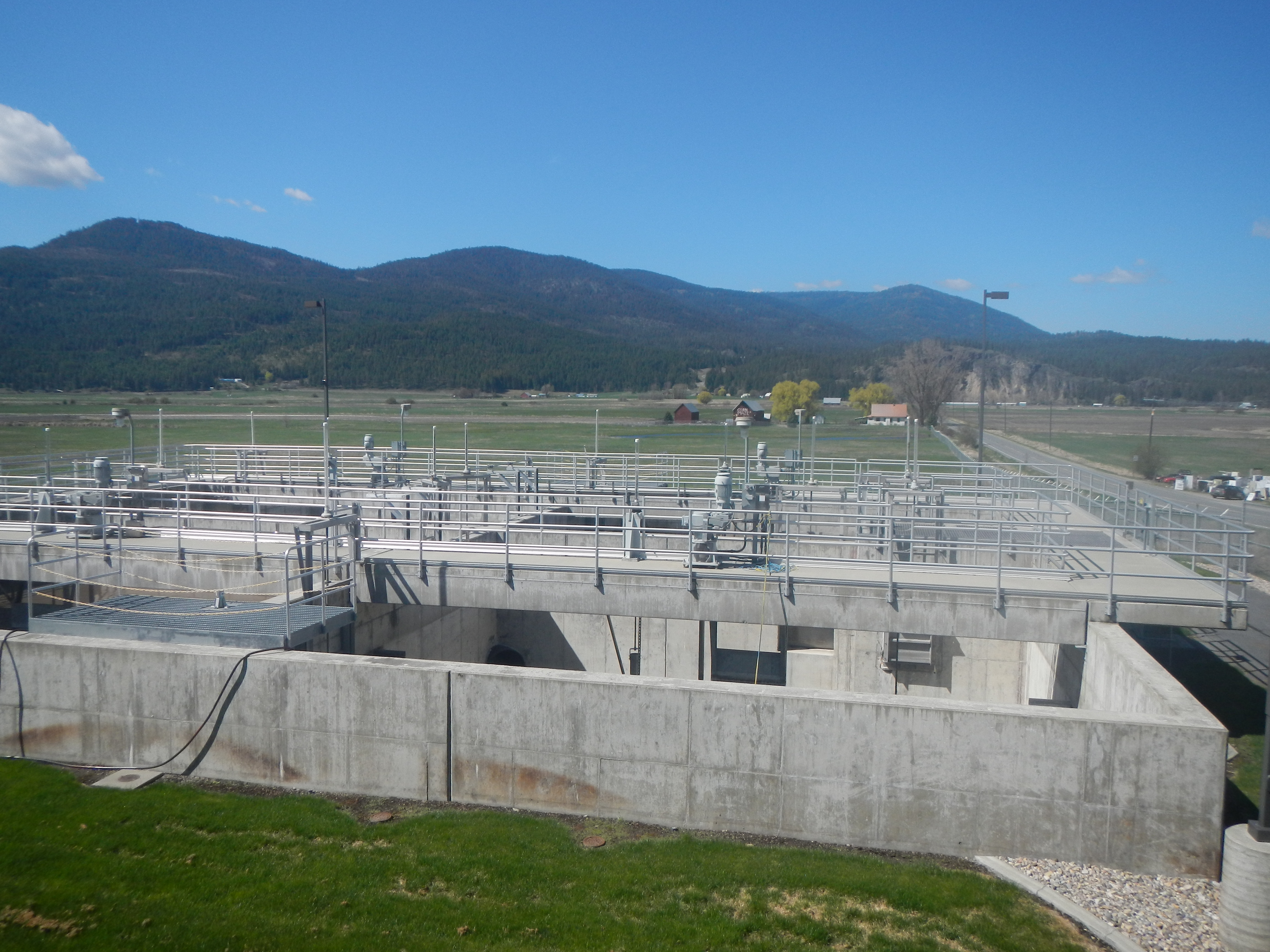 Concrete and pipes with equipment and green forested hill in background.