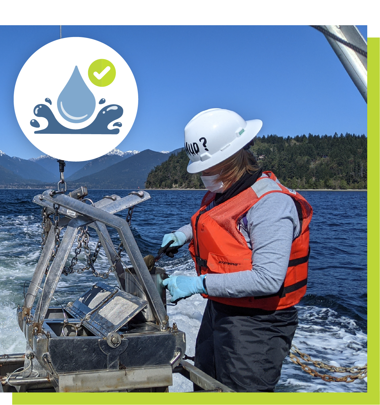 Ecology staff in a hardhat and life vest looks at sediment samples on a boat in Puget Sound, with the Olympic Mountains in the distance.
