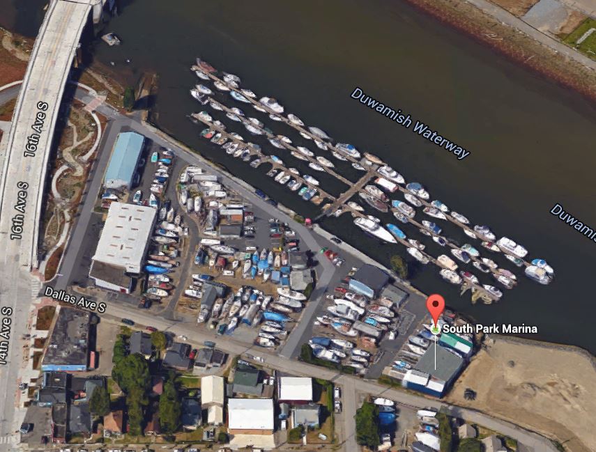 Aerial view of a riverfront marina with three T piers, plus and upland dry moorage area with boats parked on trailers.