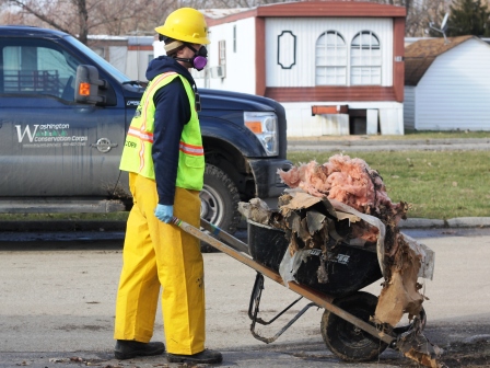 A WCC AmeriCorps member pushes a wheelbarrow full of debris pulled from a damaged structure in Missouri.