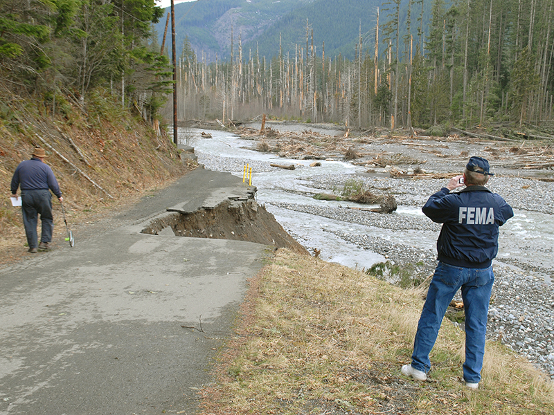 Two FEMA employees surveying a washed road, river down below them.