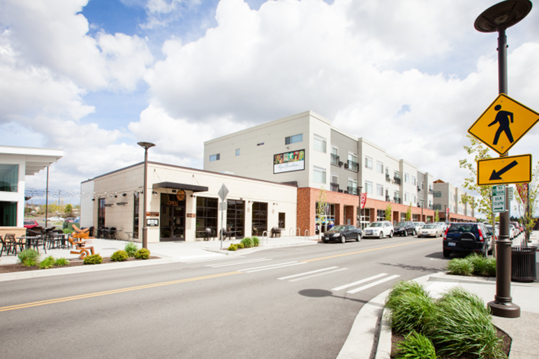 Street-level businesses with apartment housing above and a crosswalk in the foreground.