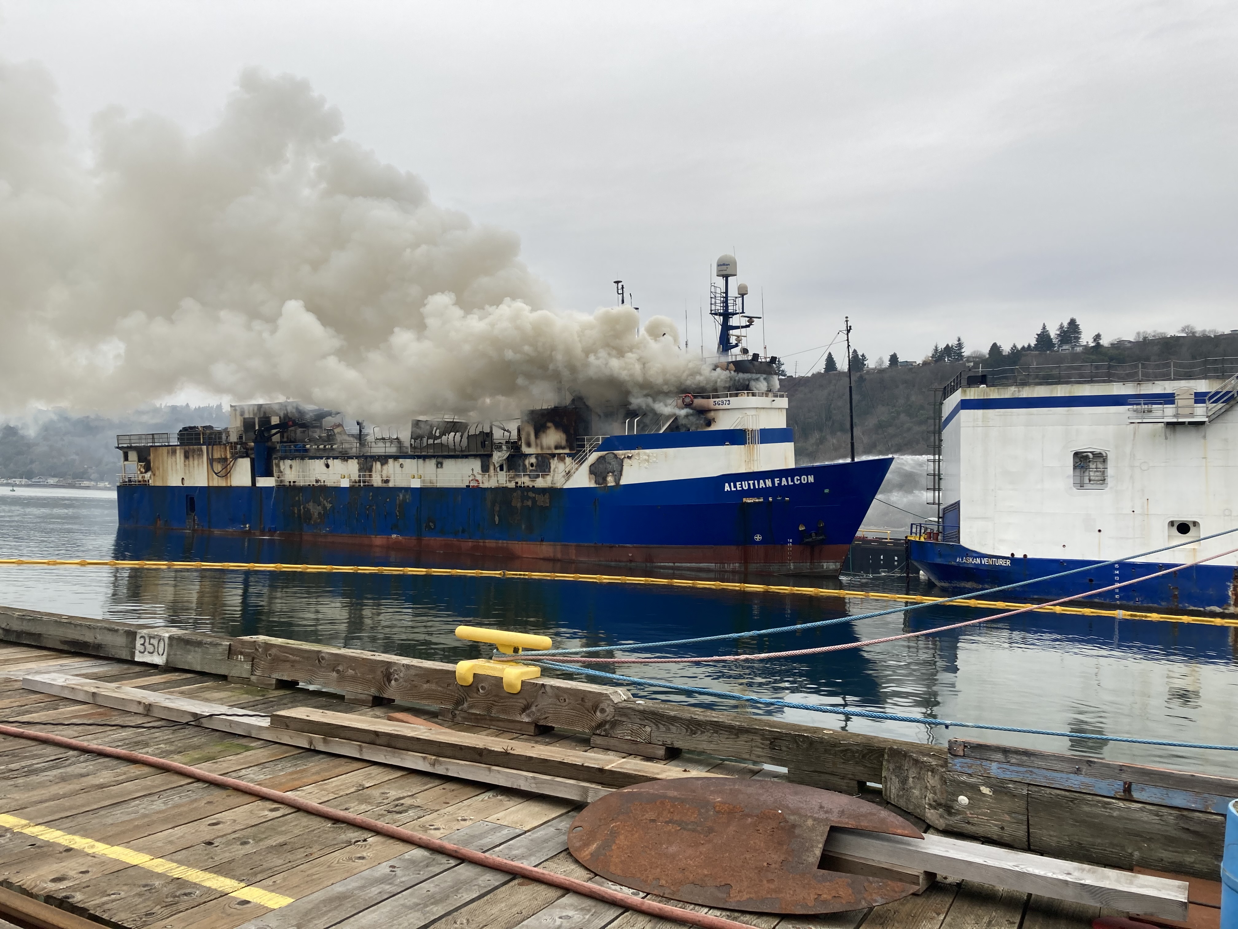 A boat on fire with smoke coming out surrounded by boom.