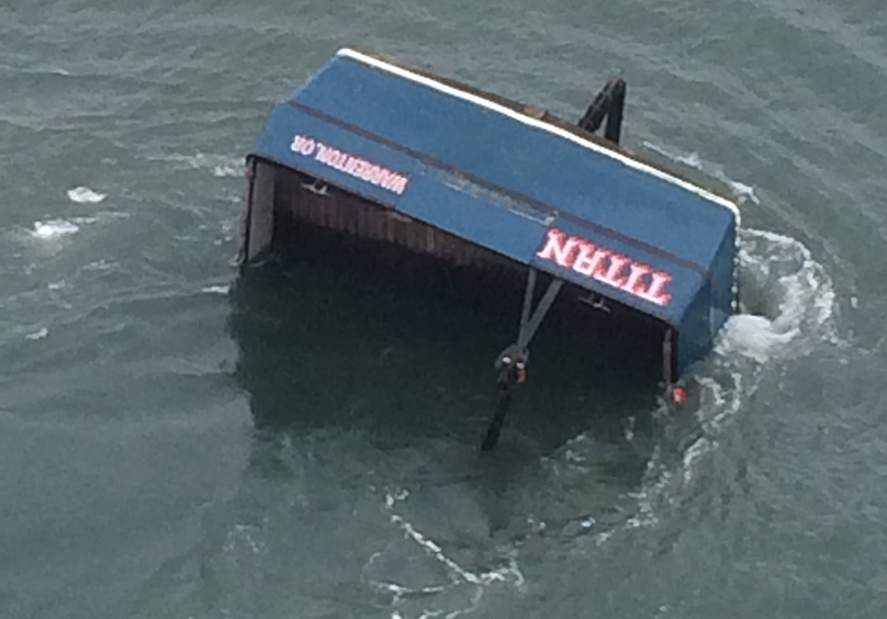 Aerial view of fishing vessel TITAN, sunk bow downward in water, with only the stern visible.