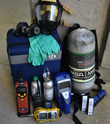 Clockwise, from top: respiratory mask and two filters, self-contained breathing apparatus (SCBA), Drager tube pump and tubes, particulate meter (blue), six-gas air monitor (yellow), hand-held radio, calibration gas canisters, volatile organic compound (VOC) and benzene monitor, chemical gloves.