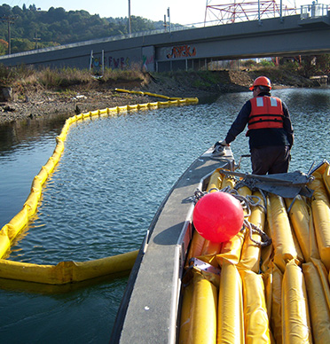 Responder deploys oil spill containment boom into water.
