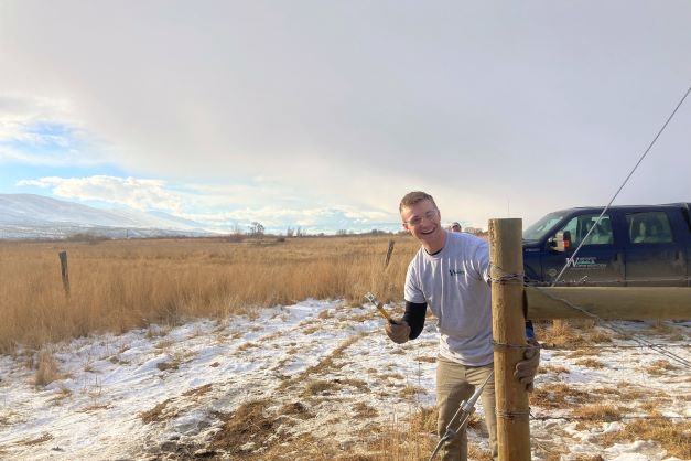 A WCC member hammers nails into a newly assembled wooden fence post.