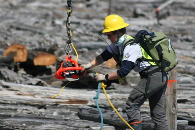 A WCC member attaches ropes to a chain hanging down from above. They are removing creosote debris from the beach.