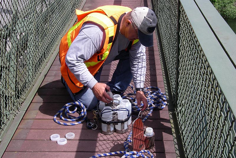 Scientist on bridge walkway prepares sampling bottles for use.