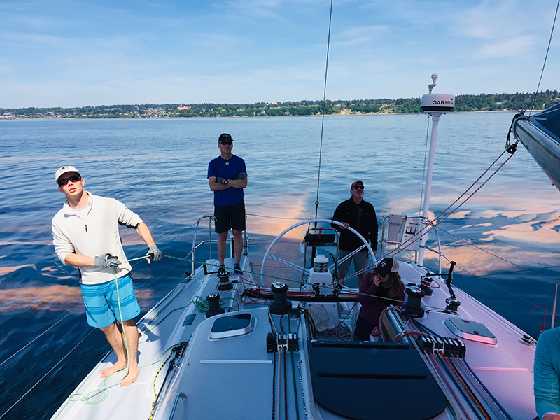 A team of sailors looks forward while orangey water trails behind