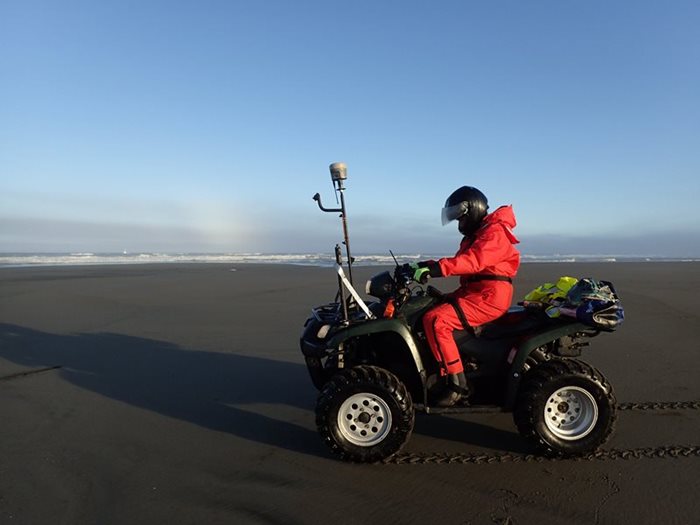 A CMAP surveyor riding on an all-terrain vehicle (ATV) on the sand collecting beach elevation data from an attached GPS unit.