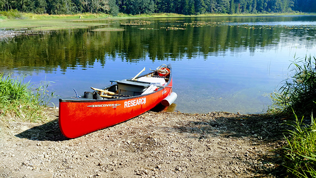 Red research canoe sits on lake edge.