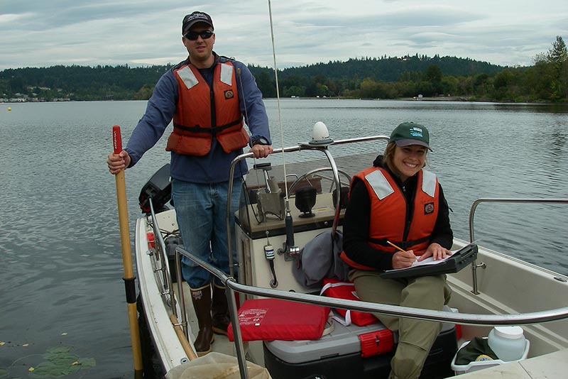 Two scientists on a small motor boat in a lake.