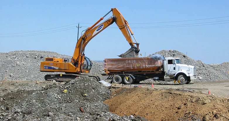 Backhoe dumps dirt into dumptruck at Hanford site.