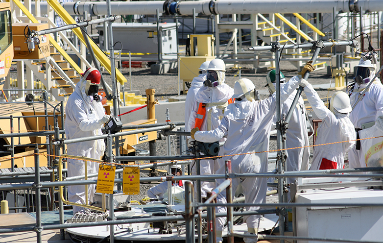 Workers examine Hanford tank equipment wearing protective suits and air masks.