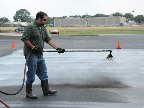 man sprays coal tar sealant in a parking lot