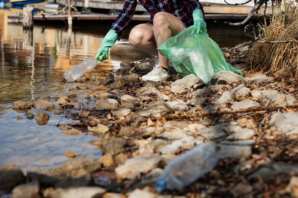 This is a decorative image of a woman picking up littered plastic bottles from a stream.