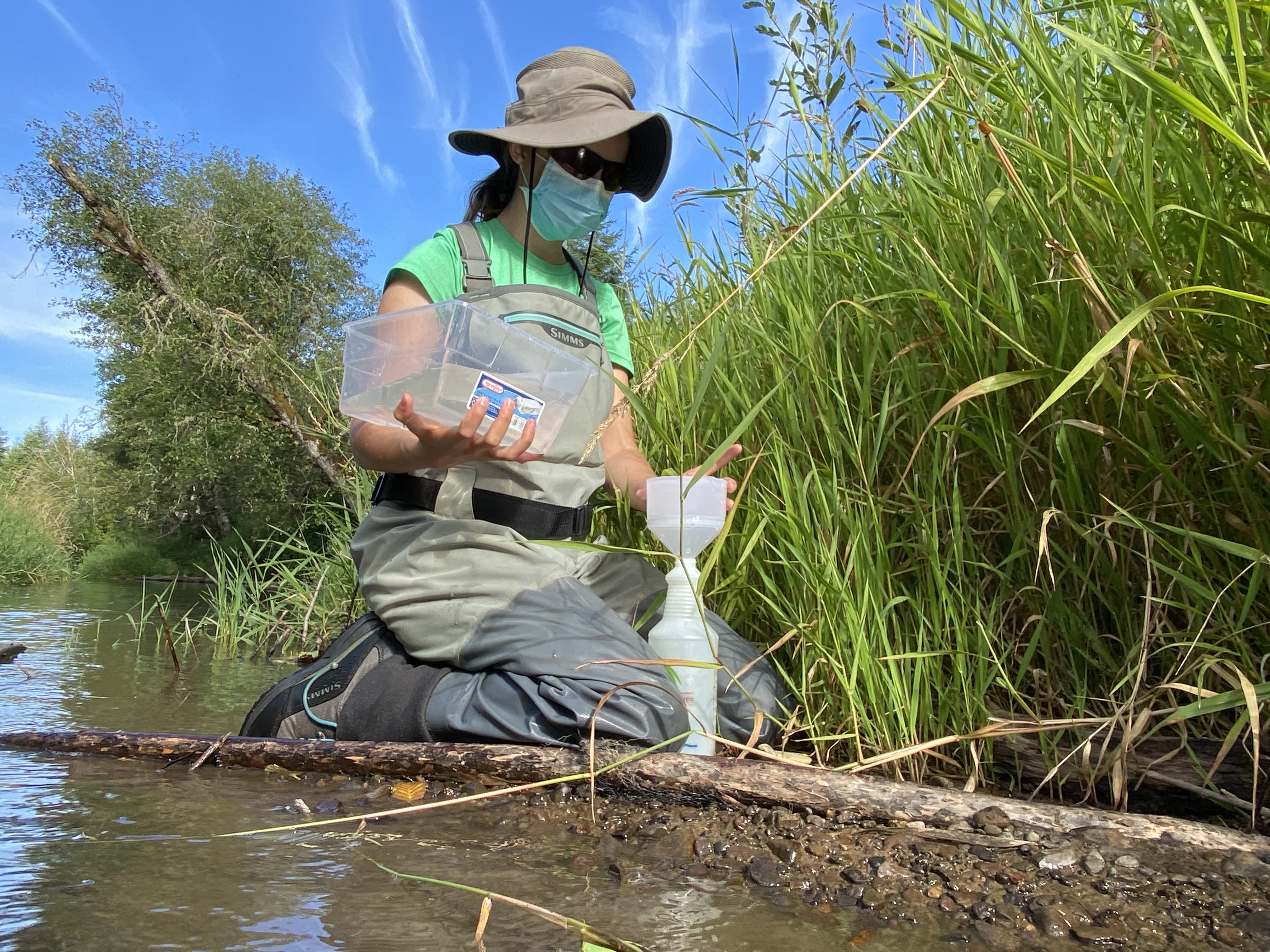 Woman kneeling next to stream holding water sampling bottle