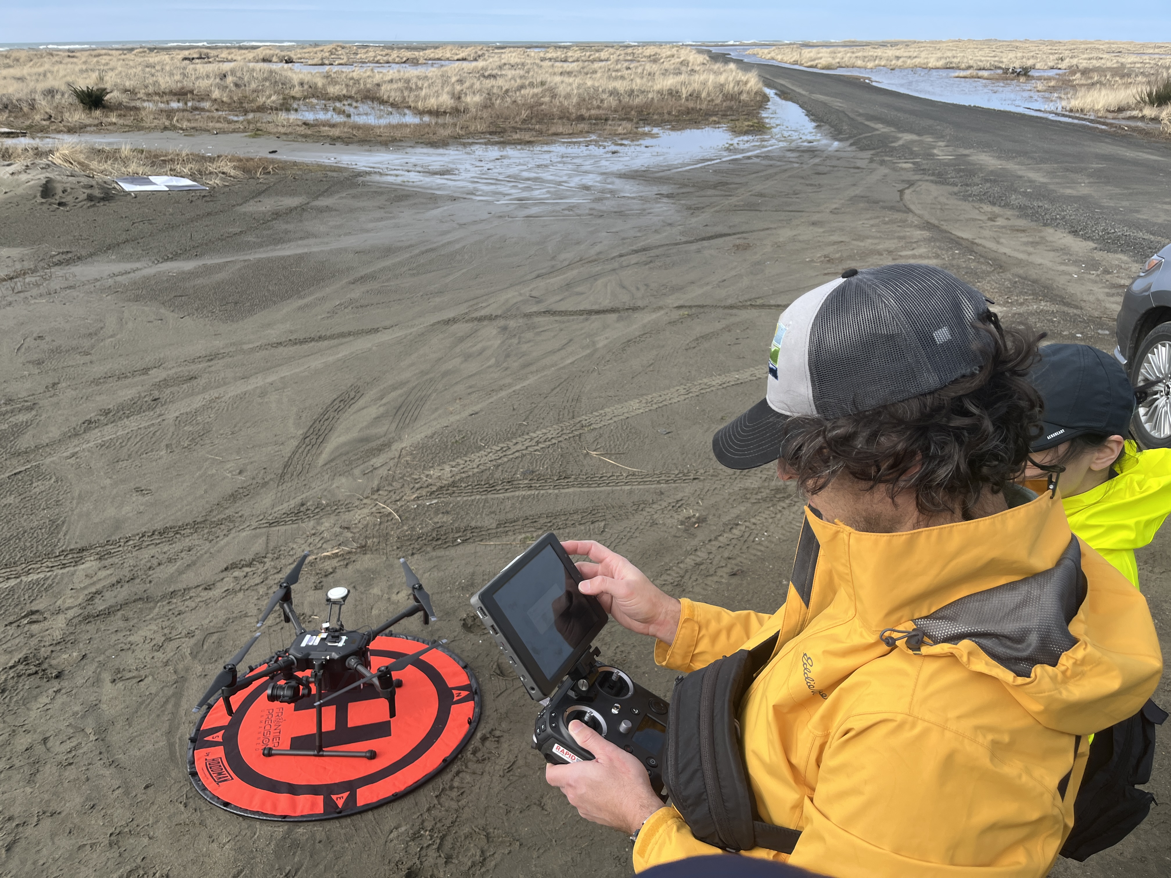 Surveyor operating tablet that controls a small drone, which is sitting on a small orange launch pand