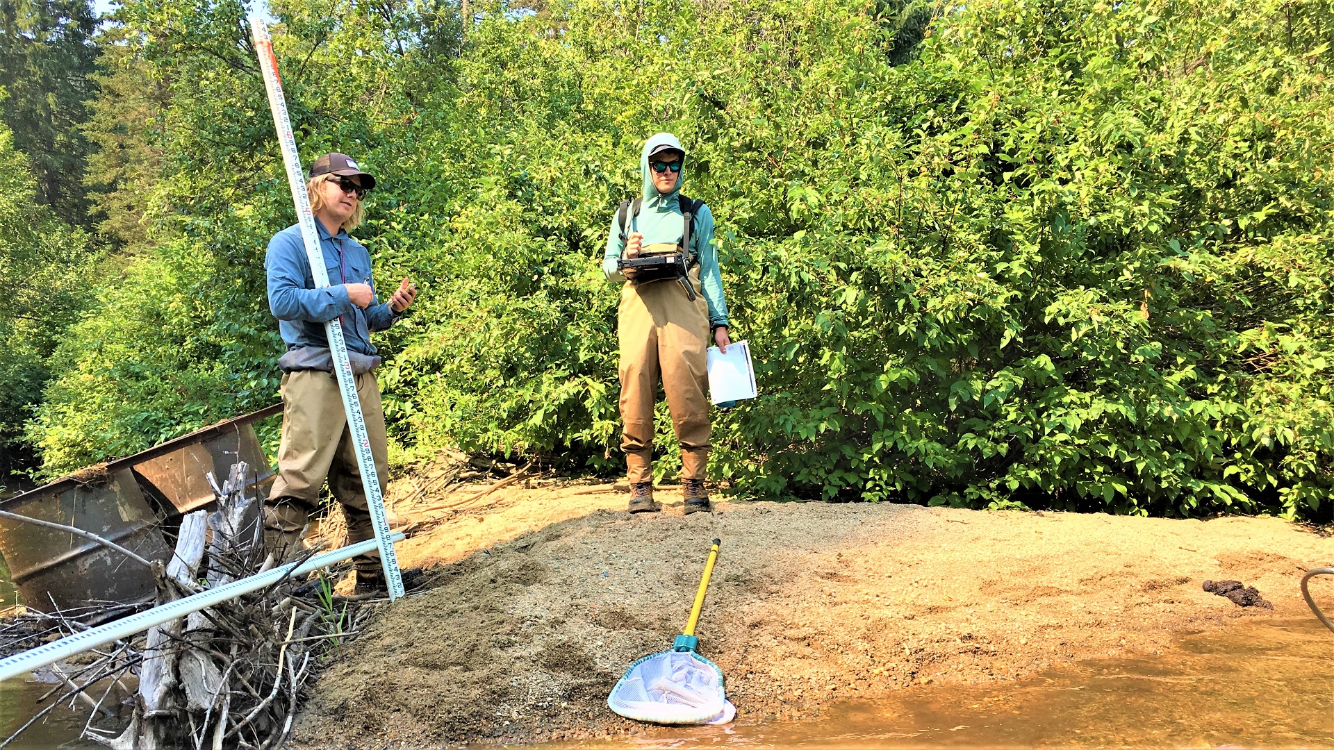 Crewmembers standing next to trash on a stream bank.