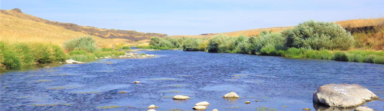 Large river surrounded by dry grassy hills.