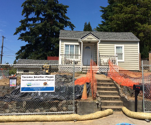 House with bare dirt yard surrounded in chainlink fence. Sign on fence says 